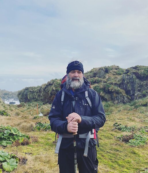 Expeditioner standing at the top of a hill in his hiking gear, smiling to camera
