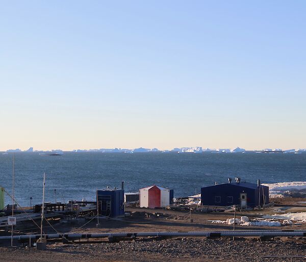 A group of small buildings in the foreground with the sea and ice bergs in the distance
