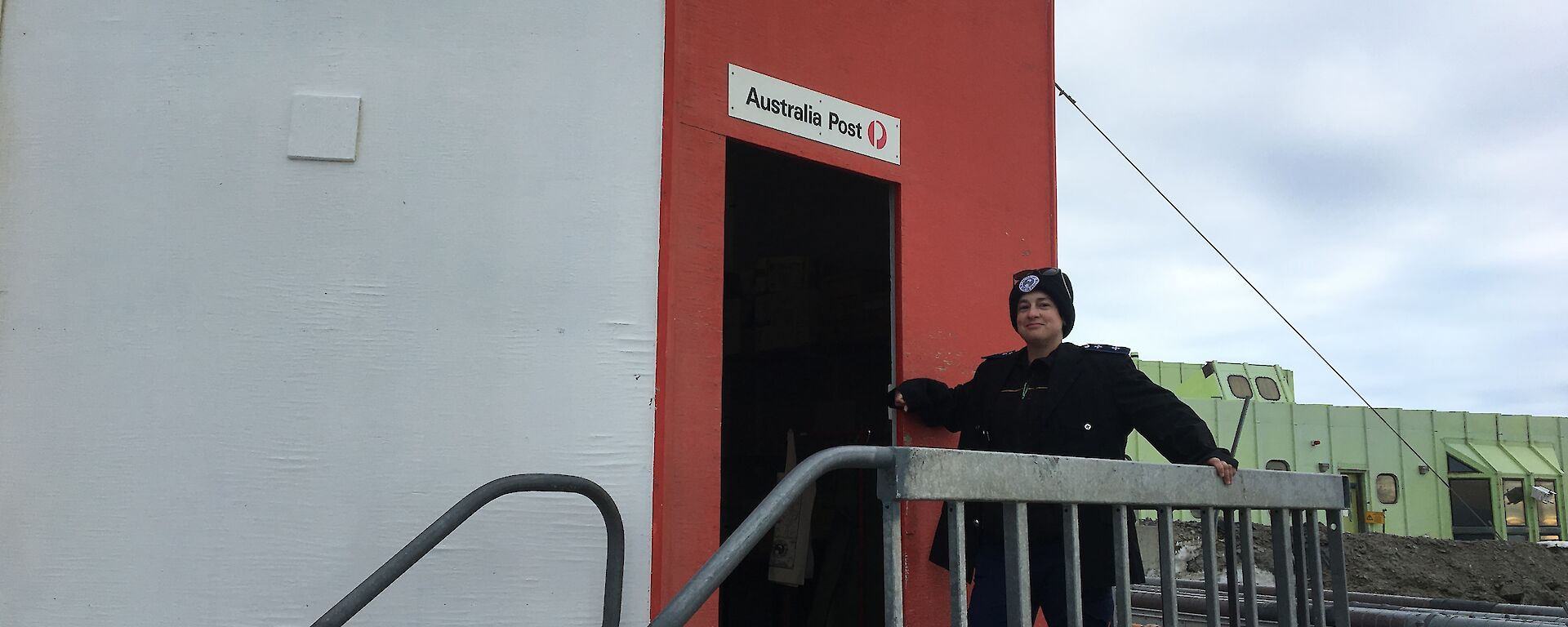 The postmaster standing at top of some stairs leading in to the red post office hut