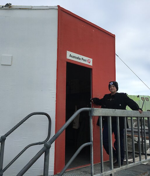 The postmaster standing at top of some stairs leading in to the red post office hut