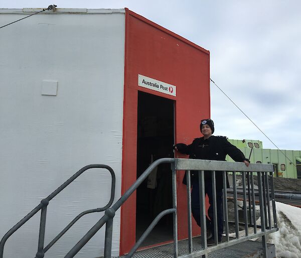 The postmaster standing at top of some stairs leading in to the red post office hut
