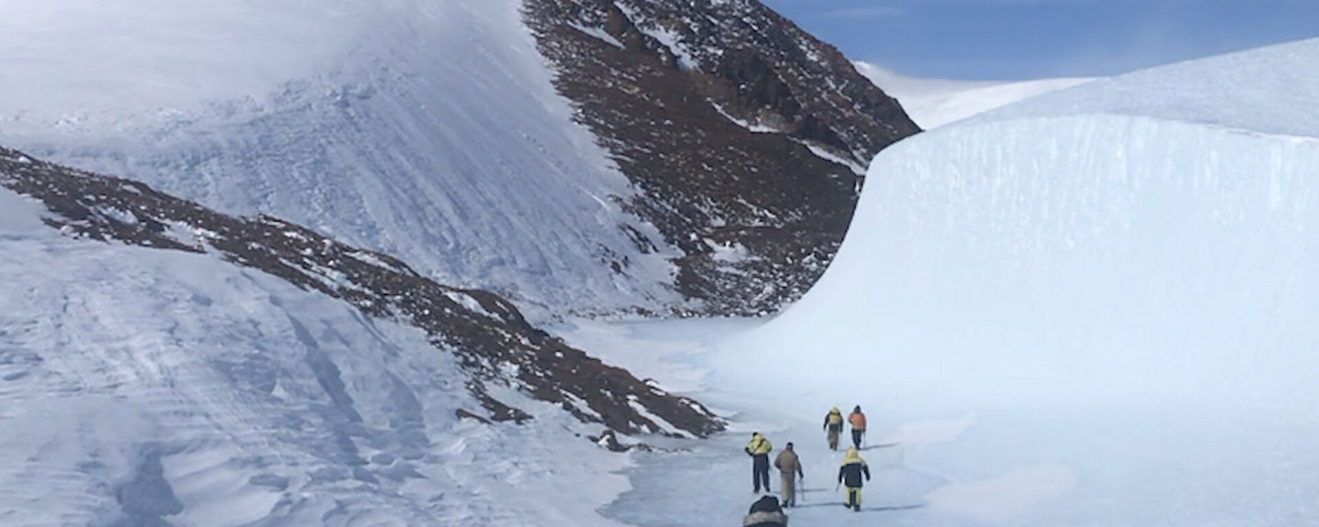 A group of expeditioners walking away from camera towards a snow mountain peak