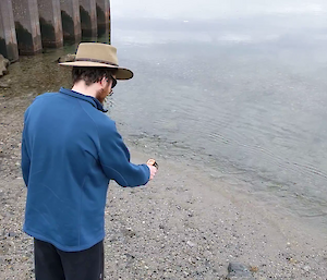 An expeditioner stands at the shoreline and looks at a thermometer