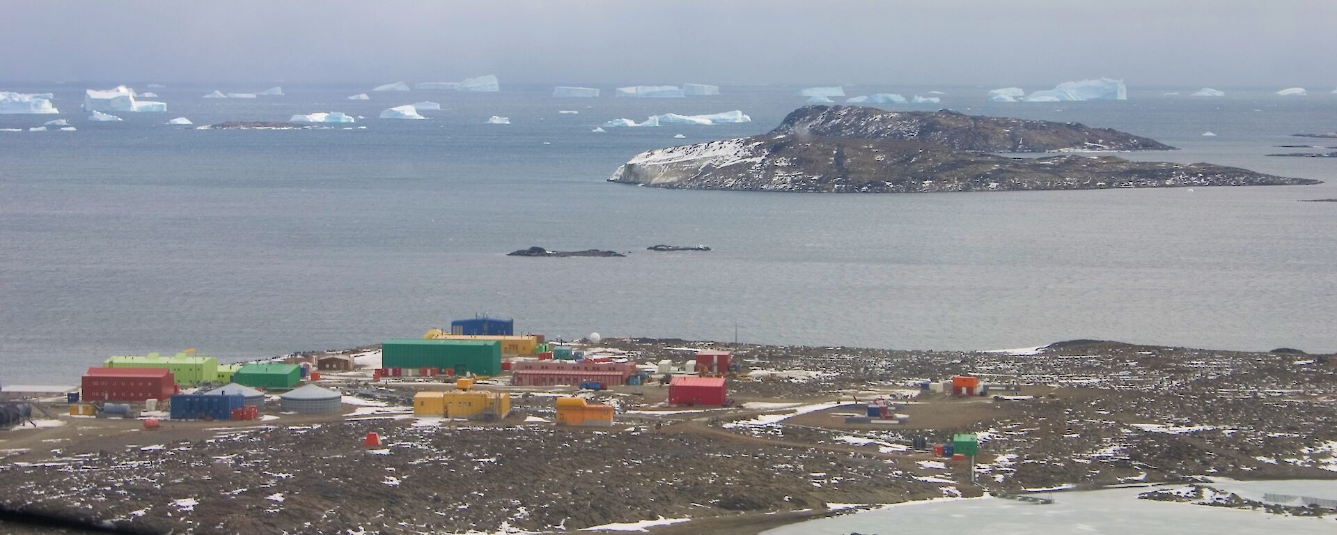 coloured buildings of an Antarctica station with sea and ice bergs behind