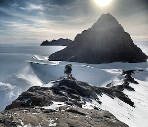 An expeditioner walking across a snowy mountain ridge towards the tip of a mountain