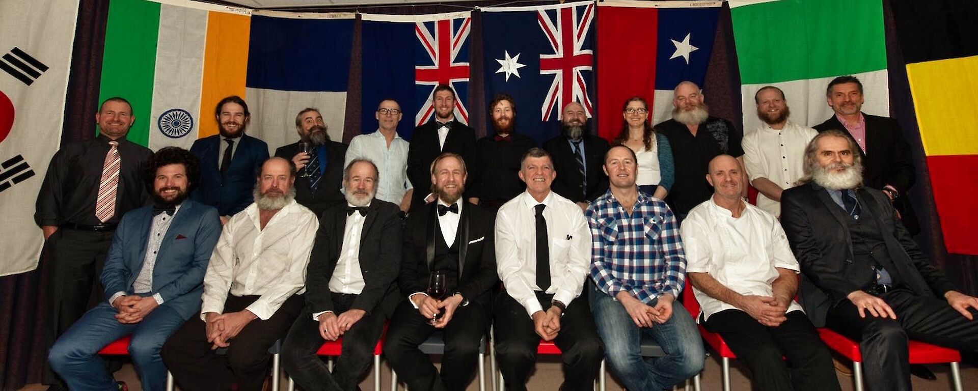 The expeditioners in a staged formal group photo with international flags in the background