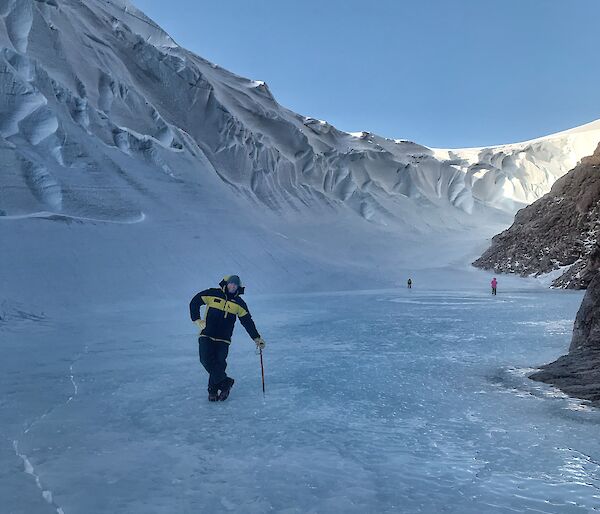 Expeditioner leaning on a walking stick while standing on the ice in the middle of an ice covered canyon.