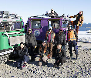 Nine women standing beside and on a purple Hagglund smiling to camera.  Snow and ice in the background