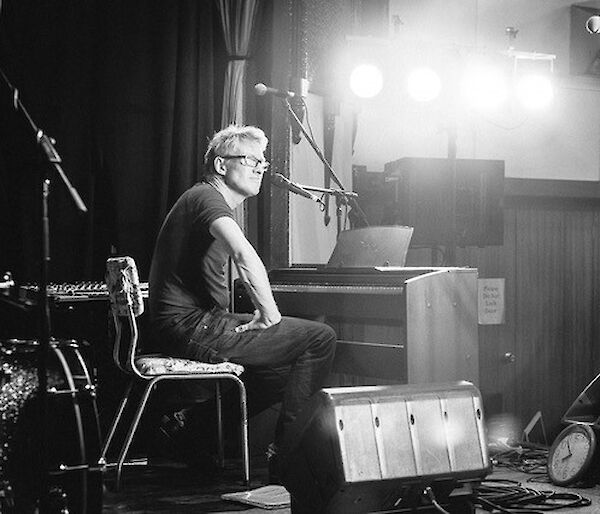 Man seated on a chair in front of a piano