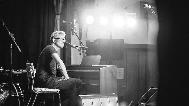 Man seated on a chair in front of a piano