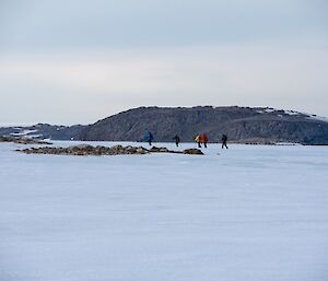 A snowy landscape with a group of colourful skiers in the distance, skiing away from camera