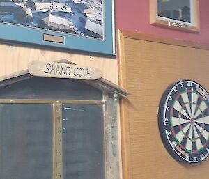 A dartboard and scoreboard on a wall with photos hung above them
