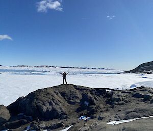 A climber standing on top of a ridge with hands up in the air in celebration.  Behind her there is ice and snow as far as the horizon.