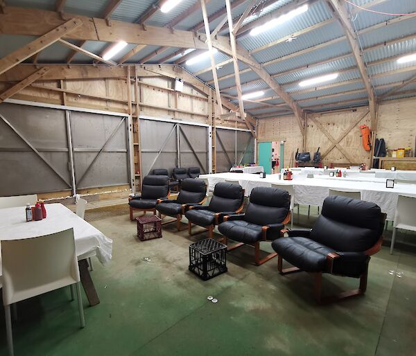 A large shed with astro turf flooring, containing dining tables set with white table cloths and 5 loungers