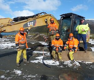 5 tradies standing in front, or sitting on a Caterpillar digger facing the camera and smiling.