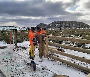 Two tradesmen working on a wooden fence with snow kissed landscape behind