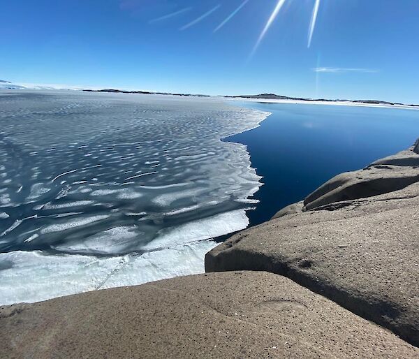Looking out across a bay with clear blue sea on one side and melting sea ice on the other