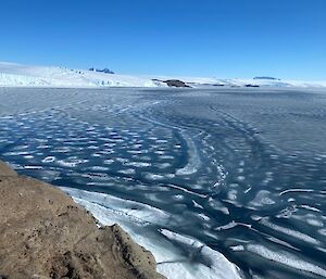 Looking out across a bay, the water full of melted ice causing beautiful patterns.  A snowly landscape on the horizon.