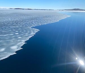 An aerial shot of the sea.  A distinct line down the middle of the shot between the clear blue sea and the melting ice.