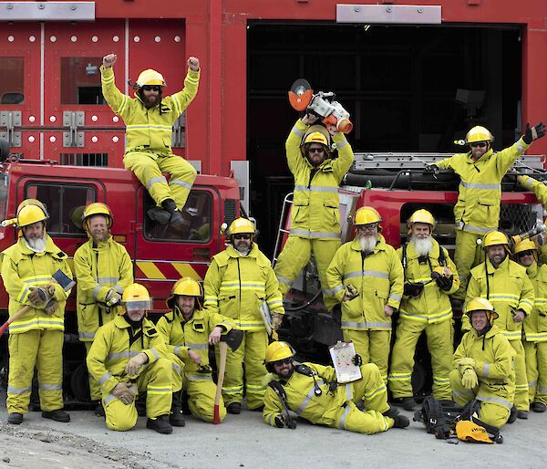 A group shot  of expeditioners in fire fighting gear standing in front of two red fire Hagglunds