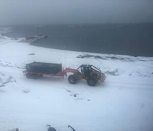 An aerial view of a loader and cargo trailer driving through the snow.