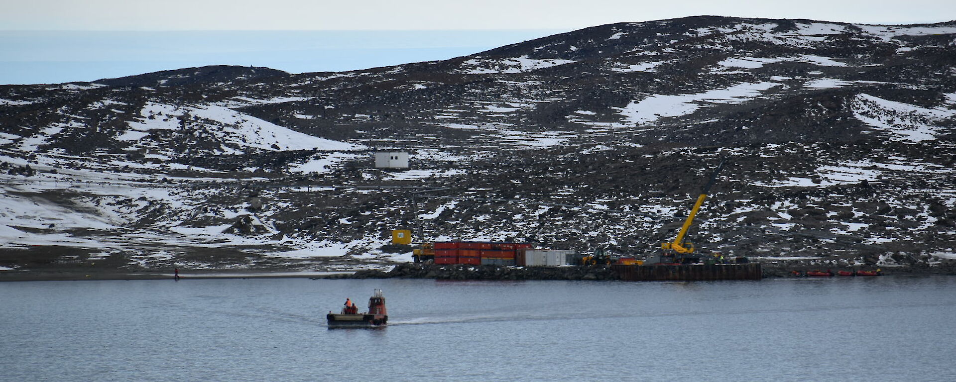 Looking out across a bay, in the middle of which sits a barge driving a load of cargo to shore