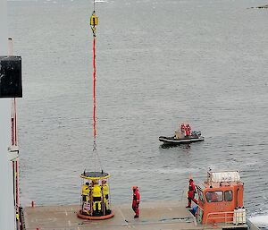 A 'Billy Pugh' lifting cage, containing 4 expeditioners, on the deck of a barge next to the ship.