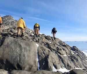 Four expeditioners make there way over a rocky outcrop surrounded by ice