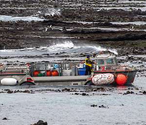 A side on shot of a  lark vessel on the sea surrounded by seaweed and rocks.  The boat has colourful buoys tied to the side and on deck.