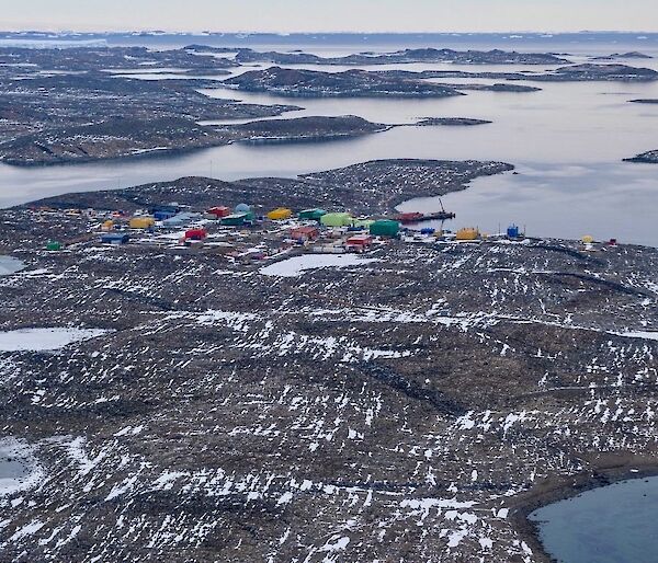 An aerial image looking down on to a group of colourful sheds and buildings situated on a snow smattered land surrounded by water