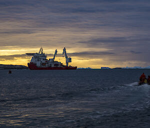 A resupply ship is visible on the horizon, silhouetted against a sunset. A dinghy heads towards them and there are icebergs on the horizon.