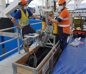 Two men on the deck of a ship with trawl equipment.