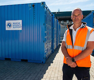 A man standing in front of a blue shipping container.