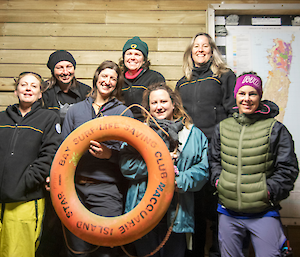 A group of women standing smiling to camera, holding an orange life ring in front of them saying 'surf life saving club Macquarie Island'