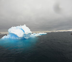 An iceberg sits in the water.  A small dinghy full of people can be seen to the right