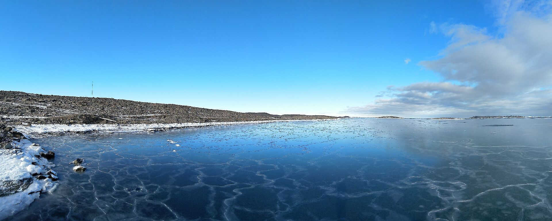 A panoramic shot of the sea ice forming at the edge of a bay with clouds gathering overhead reflected in the ice