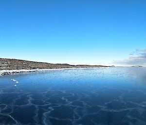 A panoramic shot of the sea ice forming at the edge of a bay with clouds gathering overhead reflected in the ice