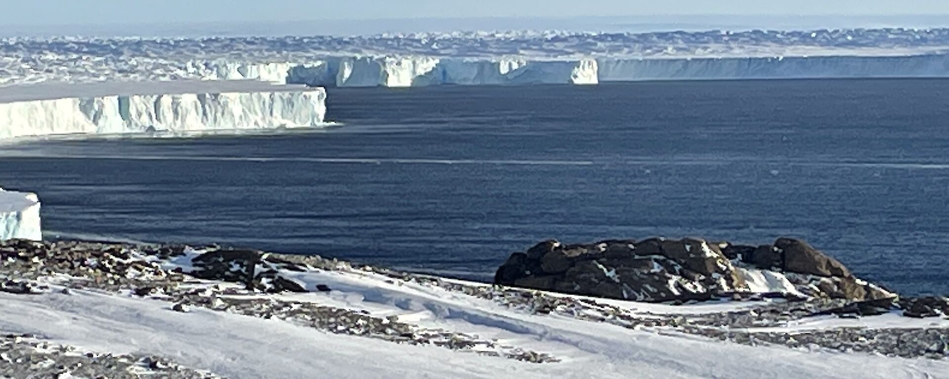 A landscape view of the snowy ground making way to the sea, and icebergs