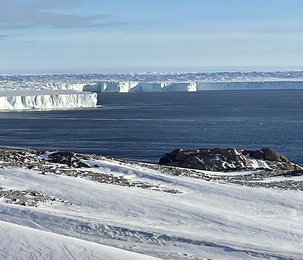 A landscape view of the snowy ground making way to the sea, and icebergs