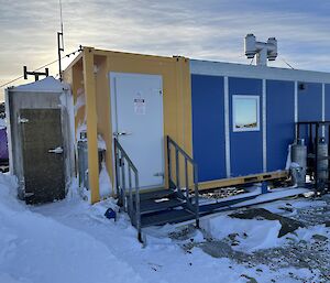 A blue shed with a yellow door frame sits in snowy ground