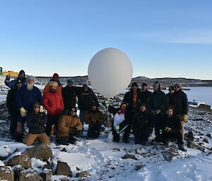 A group of people pose with a weather balloon.  Snow and ice can be seen on the ground.