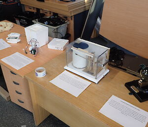 Two desks pushed together with meteorological instruments displayed with sheets of paper in front which explain what the equipment is for.