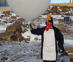 A man in a penguin suit holds a giant weather balloon ready to launch