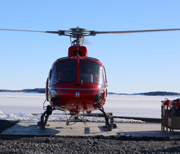 Red helicopter on the concrete landing pad with sea ice in the background.