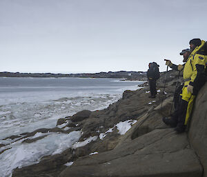 Three expeditioners standing on rocks looking over the ice
