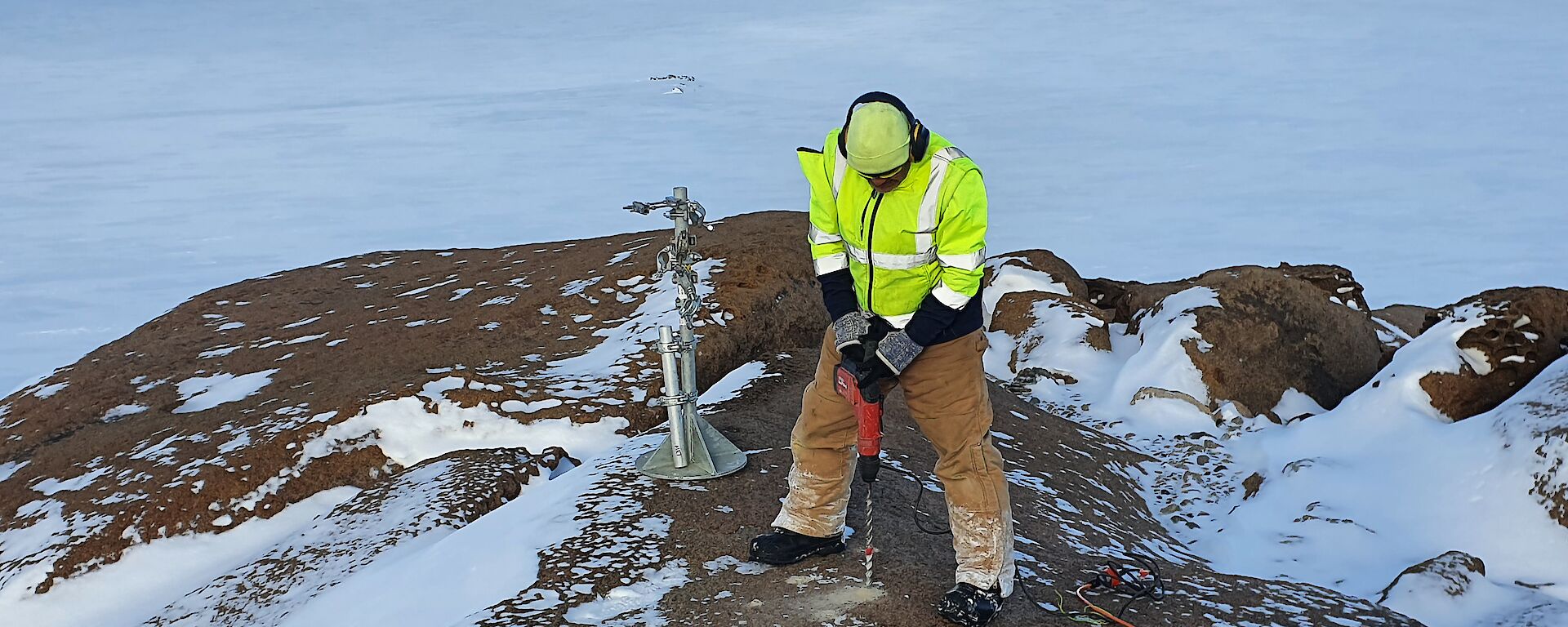 Casey expeditioner drilling a hole in the snow covered rocks for weather instruments