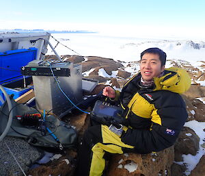 Casey expeditioner sitting on rocks while working on radio equipment