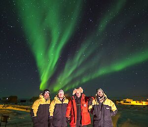 Four expeditioners pose with an aurora in the night sky