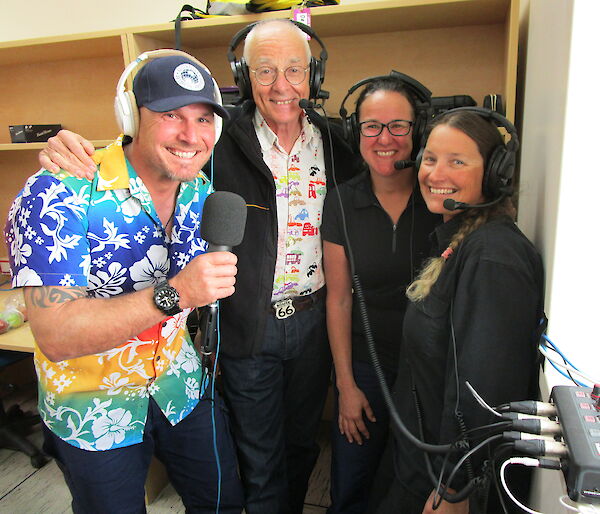 Four people looking at the camera, wearing headphones and one holding a microphone.