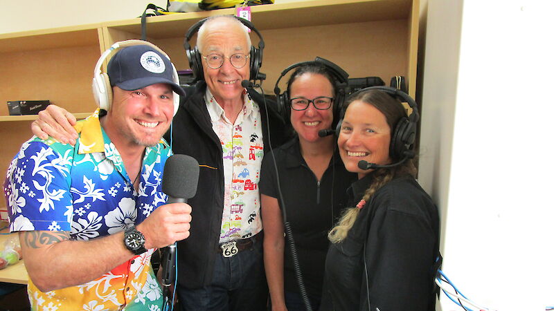 Four people looking at the camera, wearing headphones and one holding a microphone.